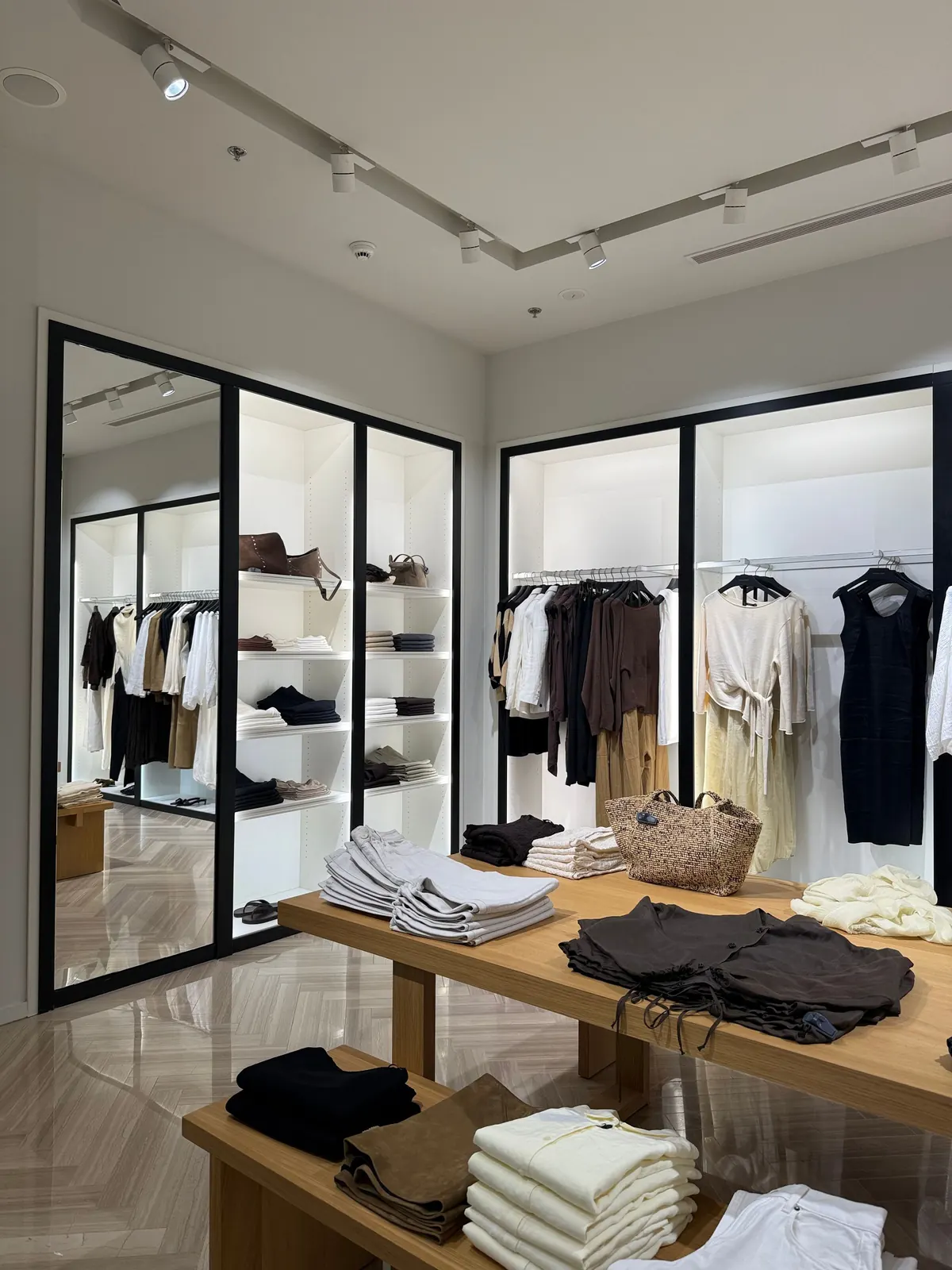 A clothing shop with black steel display cabinets, a marble floor and an oak table stacked with folded clothes.