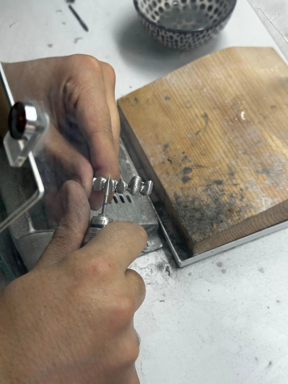 A jeweller filing a ring held in a clamp at a wooden bench.