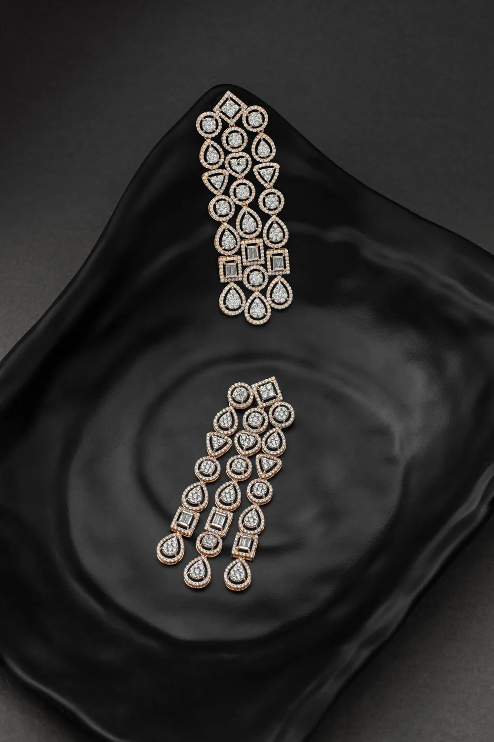 A pair of long diamond drop earrings laid on a black plate.