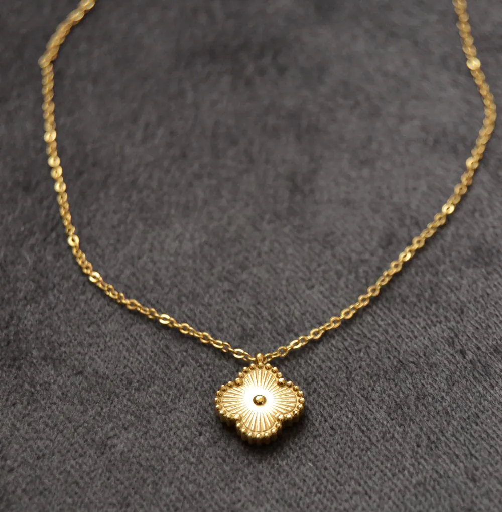 A small gold clover pendant on a fine chain, on grey velvet.