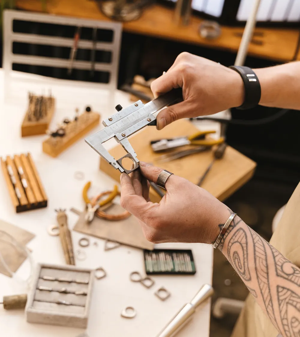 A jeweller measuring a ring with a caliper at the bench.