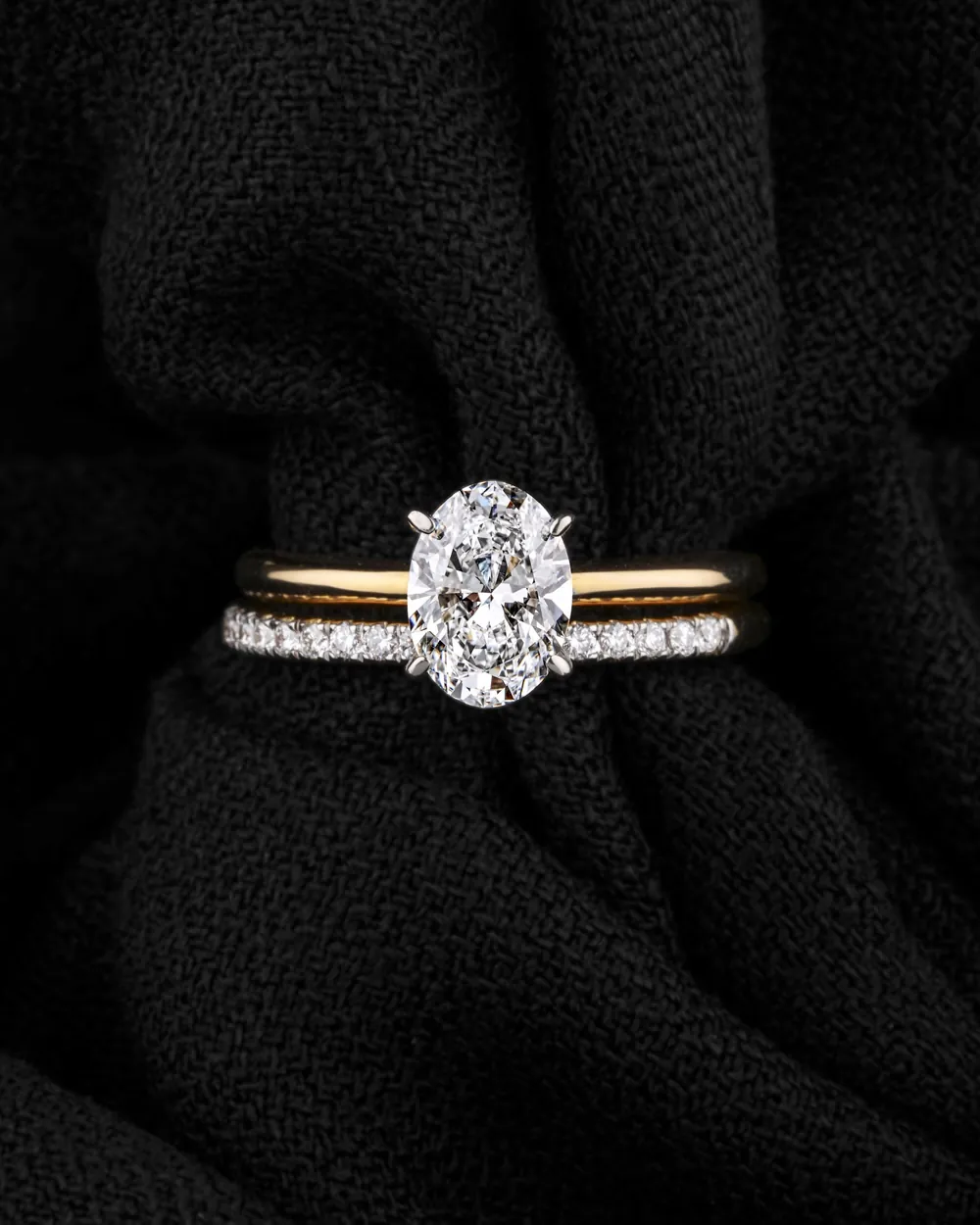 An oval diamond solitaire on a pavé band, resting on black fabric.