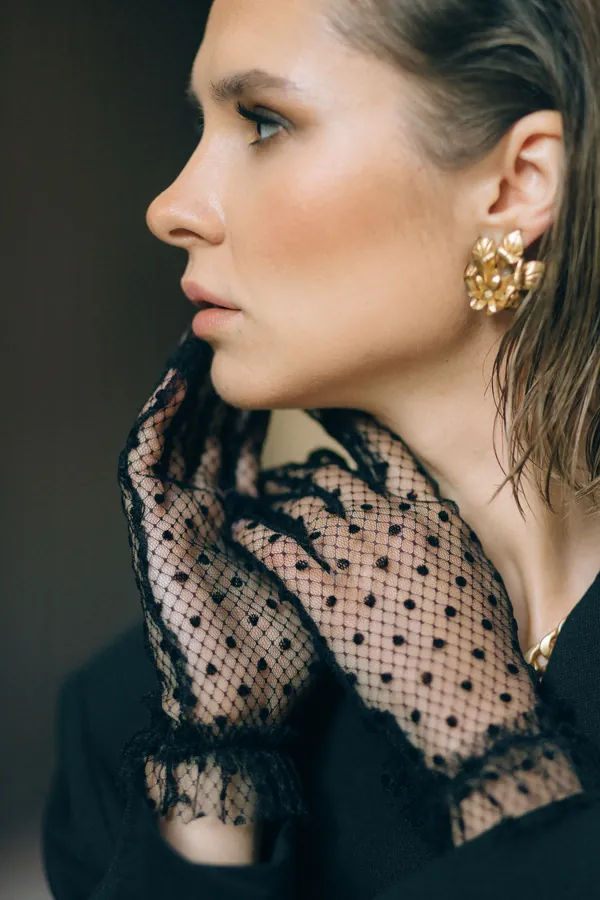 A woman in black lace gloves wearing large gold earrings.