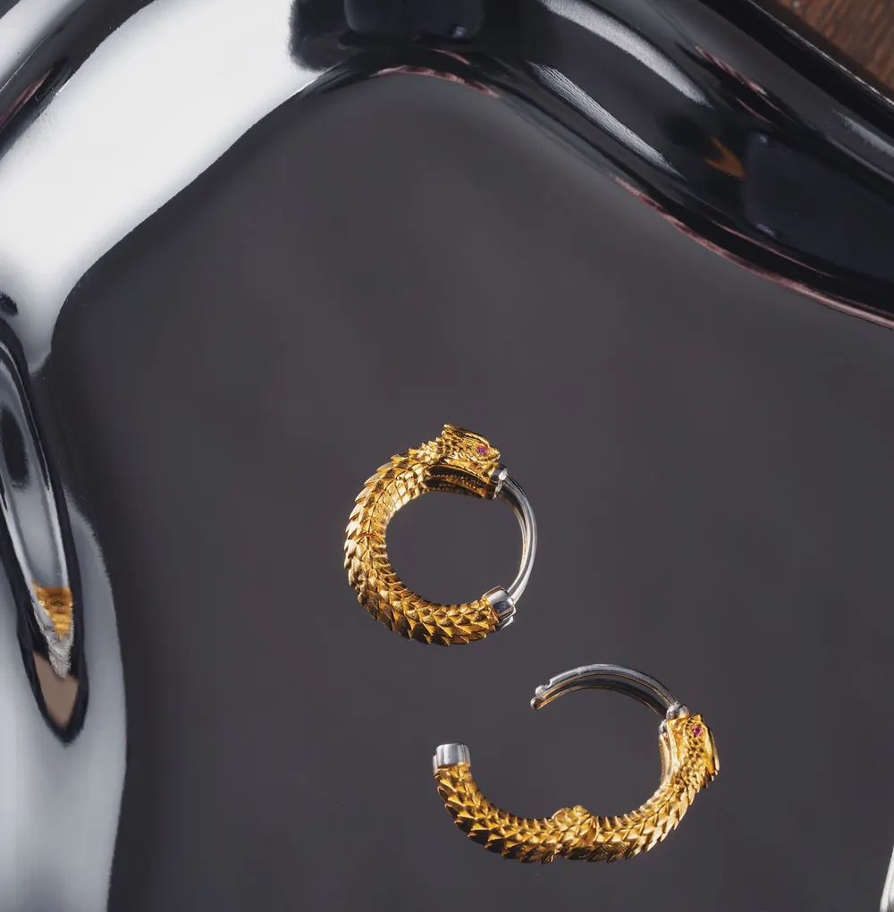 A pair of small textured gold hoops on a black tray.