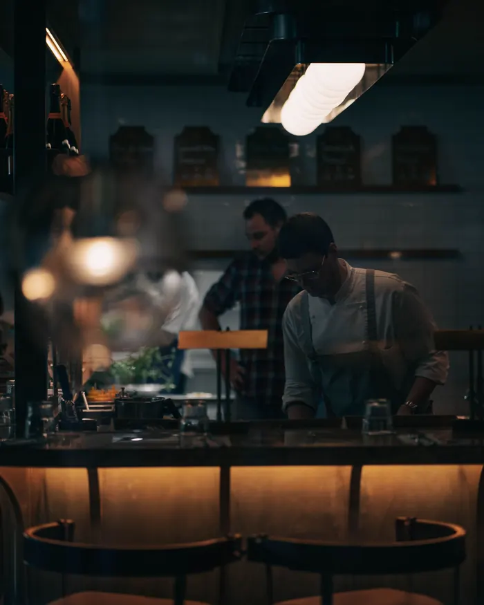 Cooks working at the pass of a dim restaurant kitchen.
