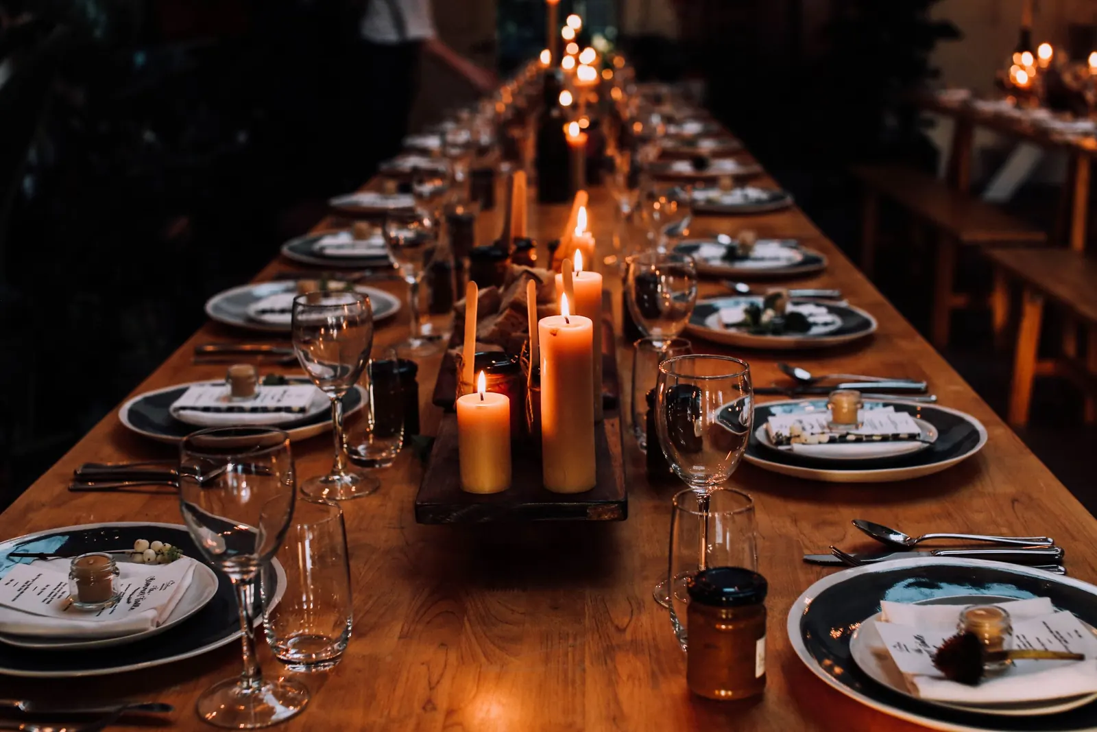 A long table set with plates, glasses and lit candles in a dark room.