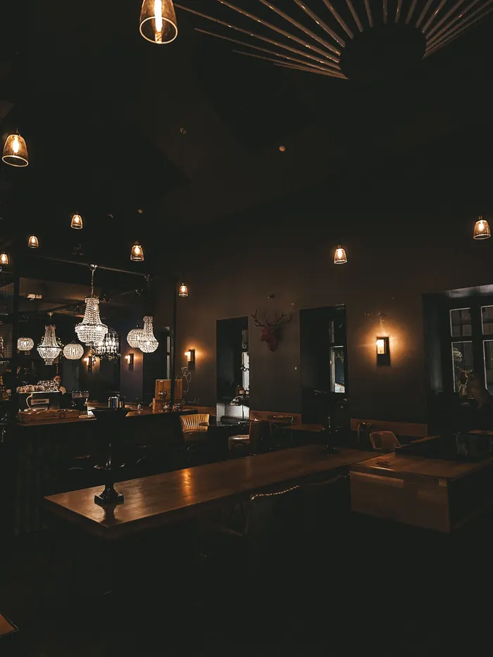 A dim dining room with small lamps on the tables and a chandelier at the back.