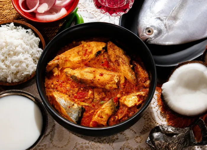 Fish curry with rice, coconut and a whole fish on the table.