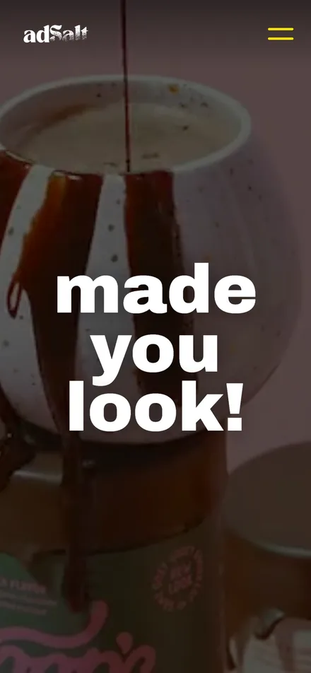 The new adSalt homepage on a phone: made you look! in big white letters over chocolate sauce running down a speckled mug, with the adSalt logo and a yellow menu button.